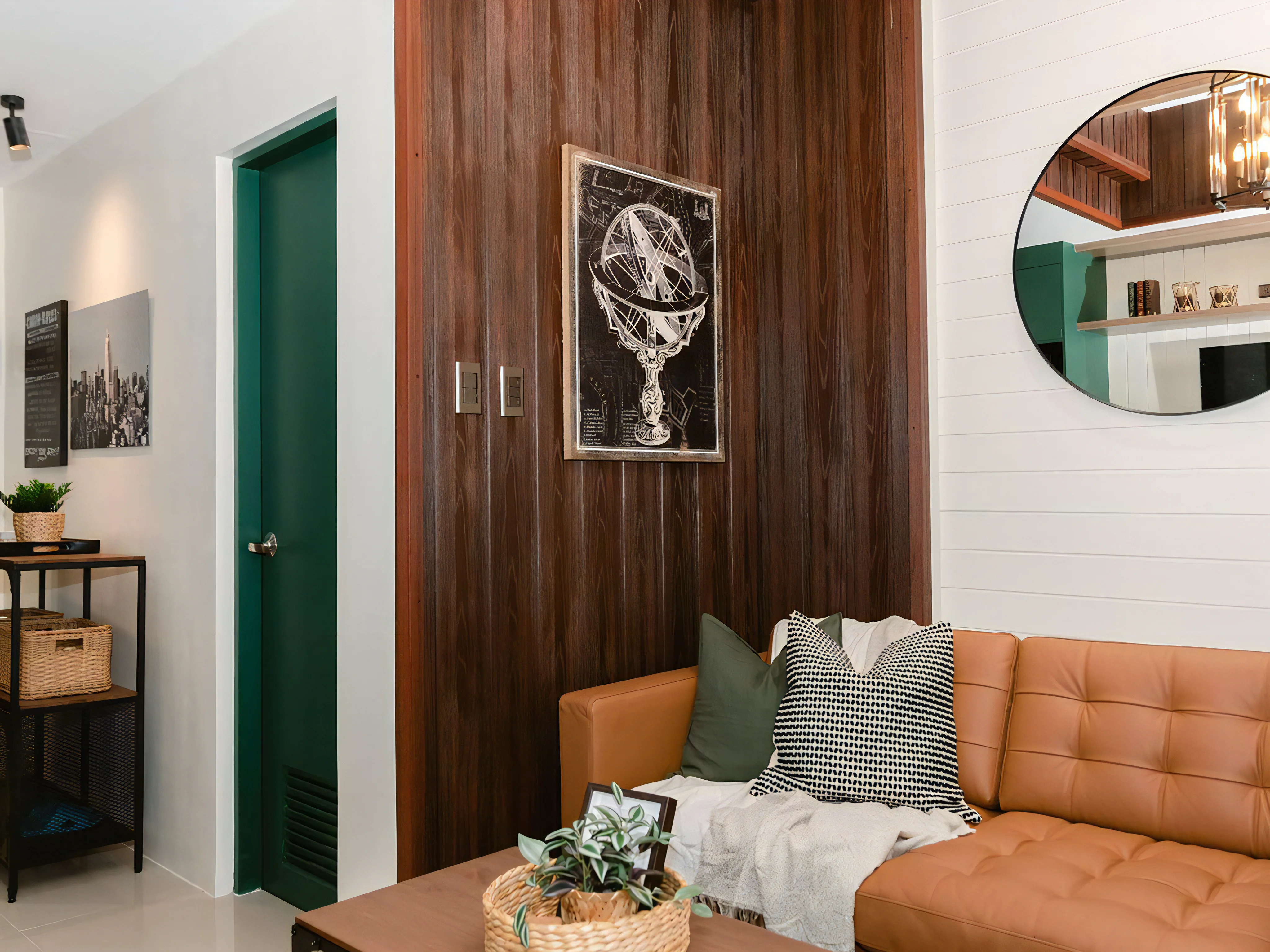 A cozy living room corner featuring a rich, dark-brown vertical wood-paneled wall. The space is decorated with a brown leather sofa, a circular mirror, and a green interior door.